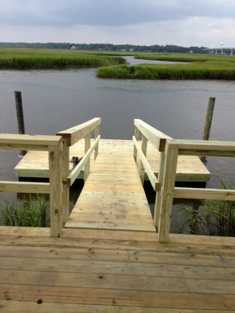 A fixed wooden pier with a T-head platform over a tidal marsh creek