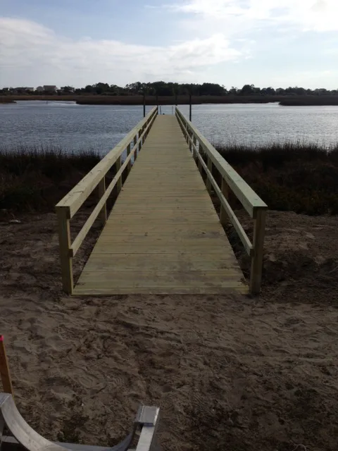 A new wooden walkway pier extending across sand to a marsh-front dock