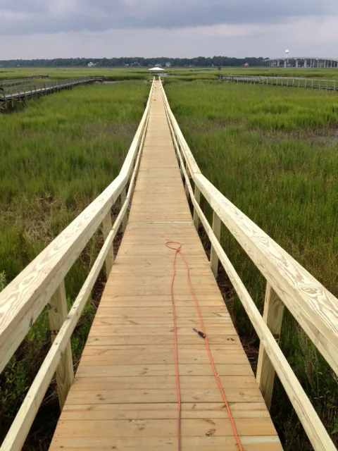 A long railed walkway pier running straight across green salt marsh