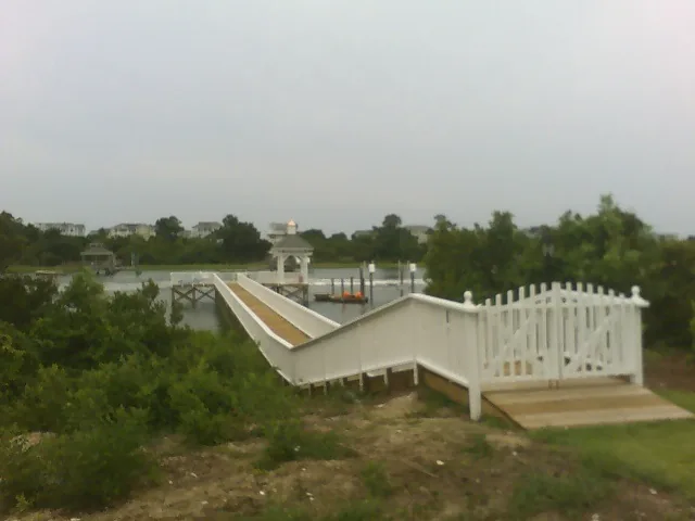 A walkway with white vinyl railings stepping down through coastal scrub toward a dock