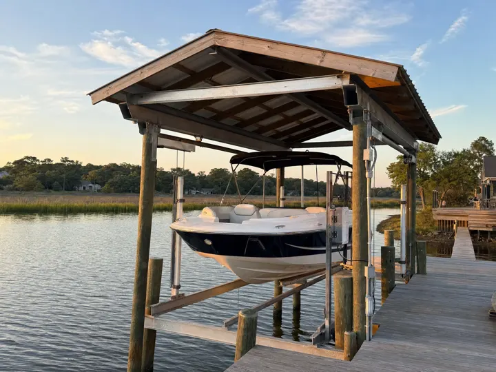 A covered boat lift holding a boat above the water beside a dock