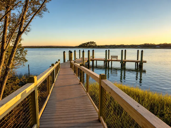 A wooden dock and pier extending over calm coastal water at golden hour